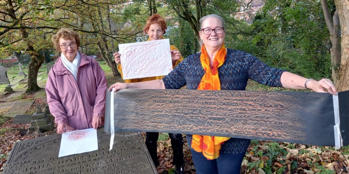 Three workshop participants holding up their finished rubbings beside the gravestones at St Mary&rsquo;s Churchyard