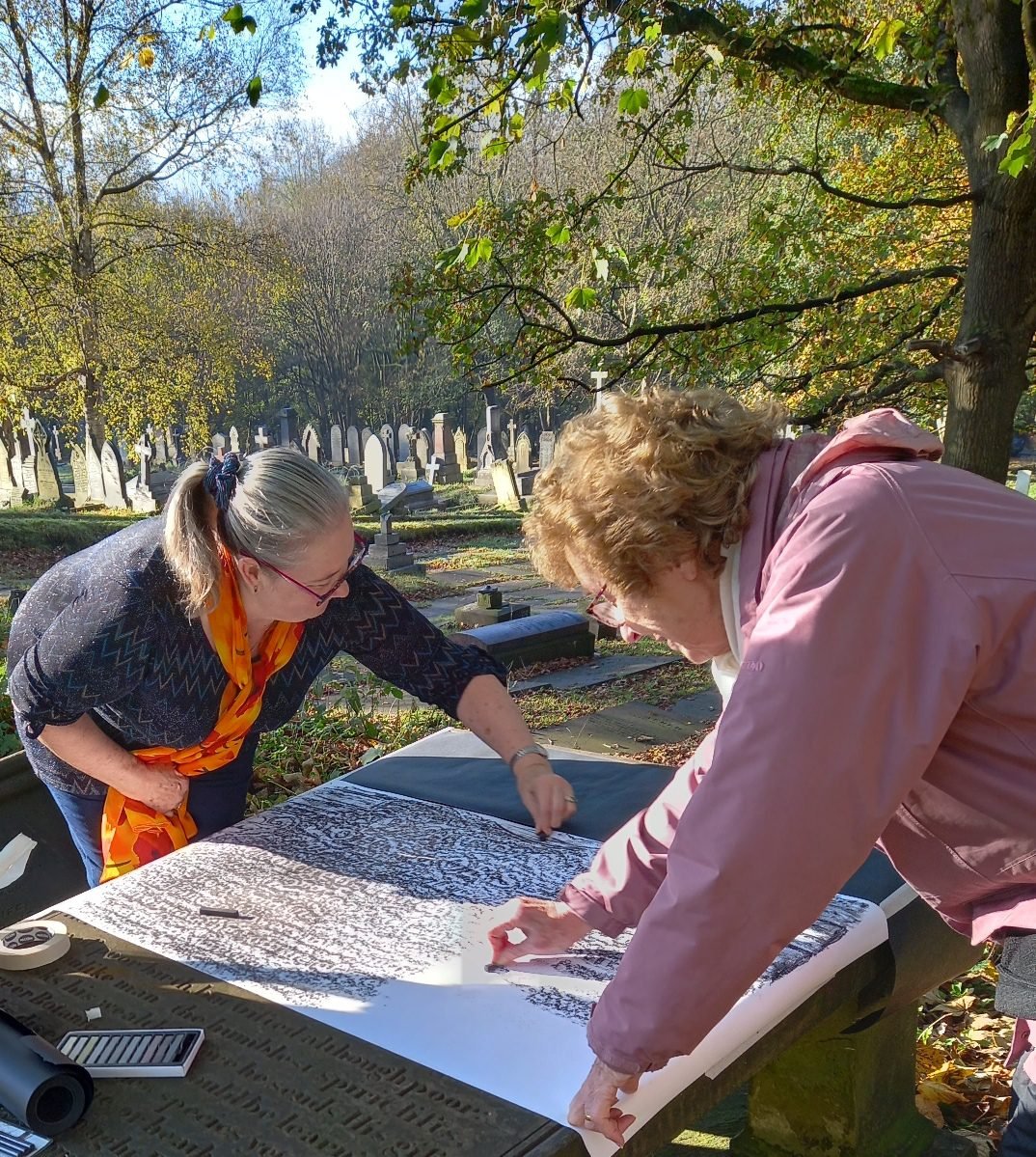 A close view of two women rubbing wax over paper laid across a large gravestone during the Artisan Naturalists workshop