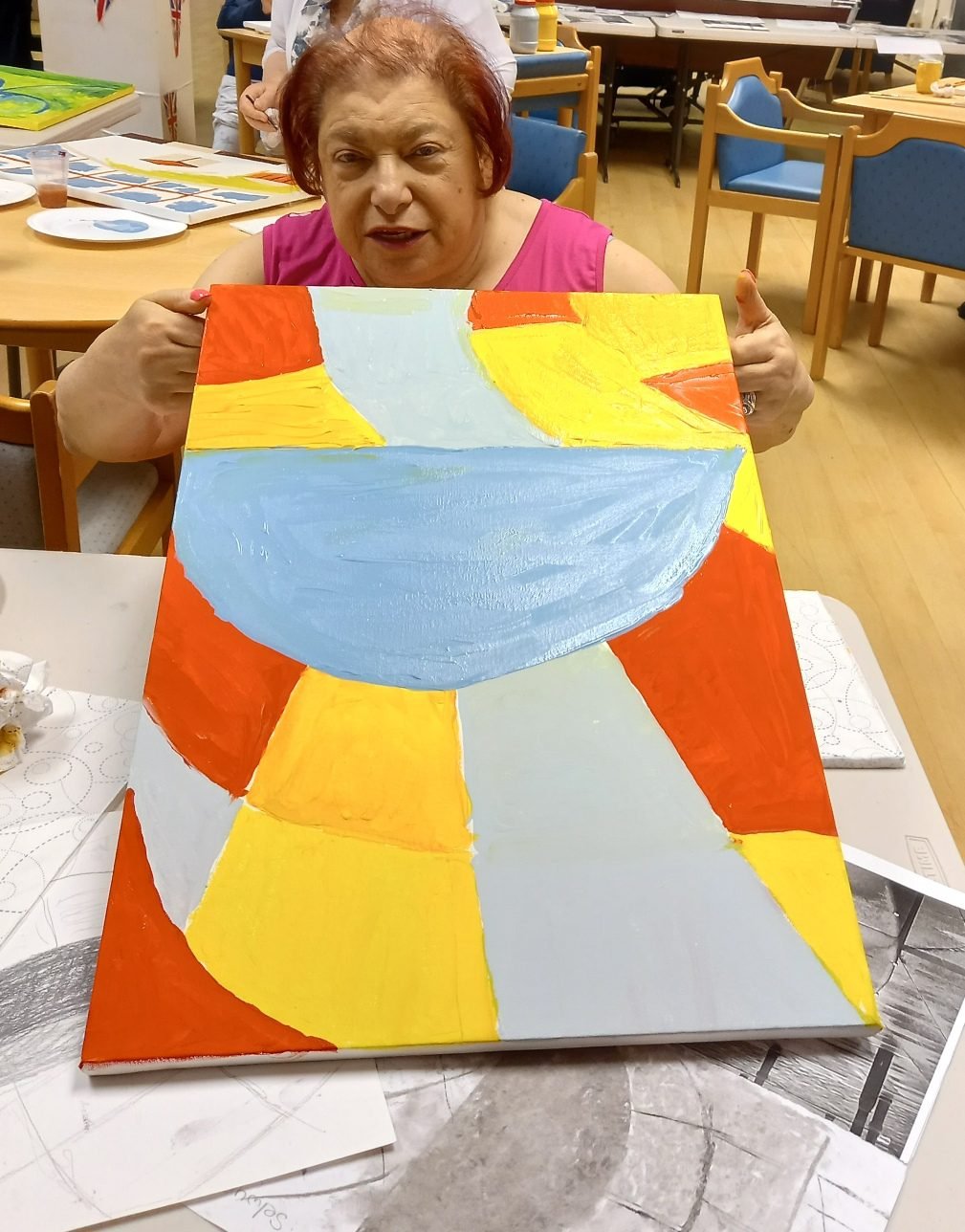 A workshop participant holding an abstract canvas in orange, yellow and pale blue Prestwich Palette tones