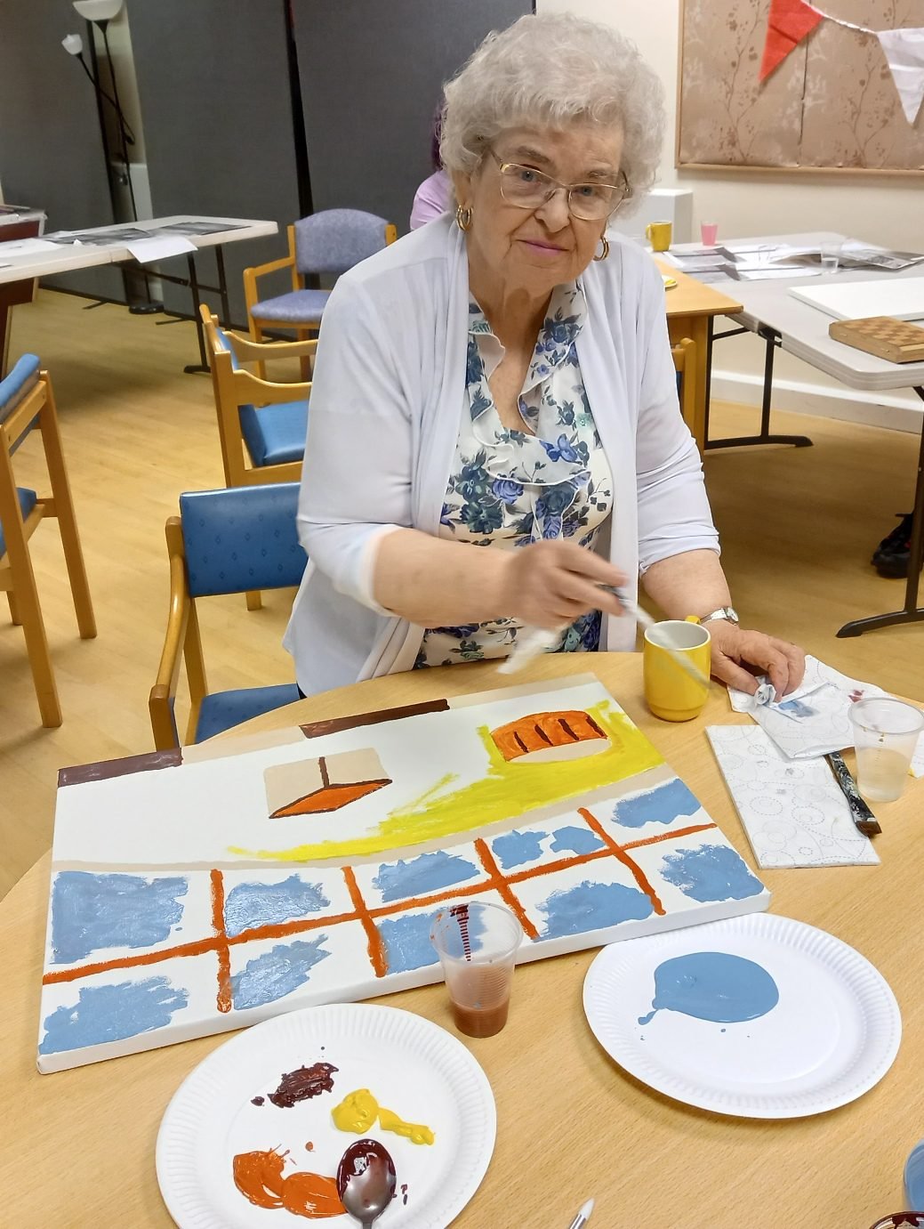 A workshop participant painting a canvas in Prestwich Palette blues and oranges at a table