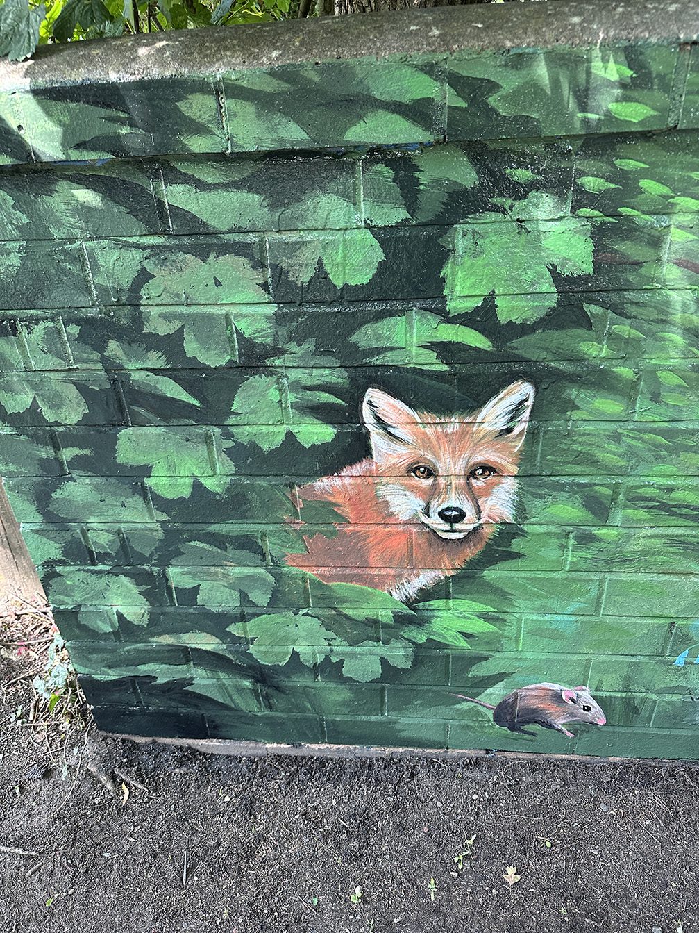 Detail of a fox peering through foliage, with a mouse below