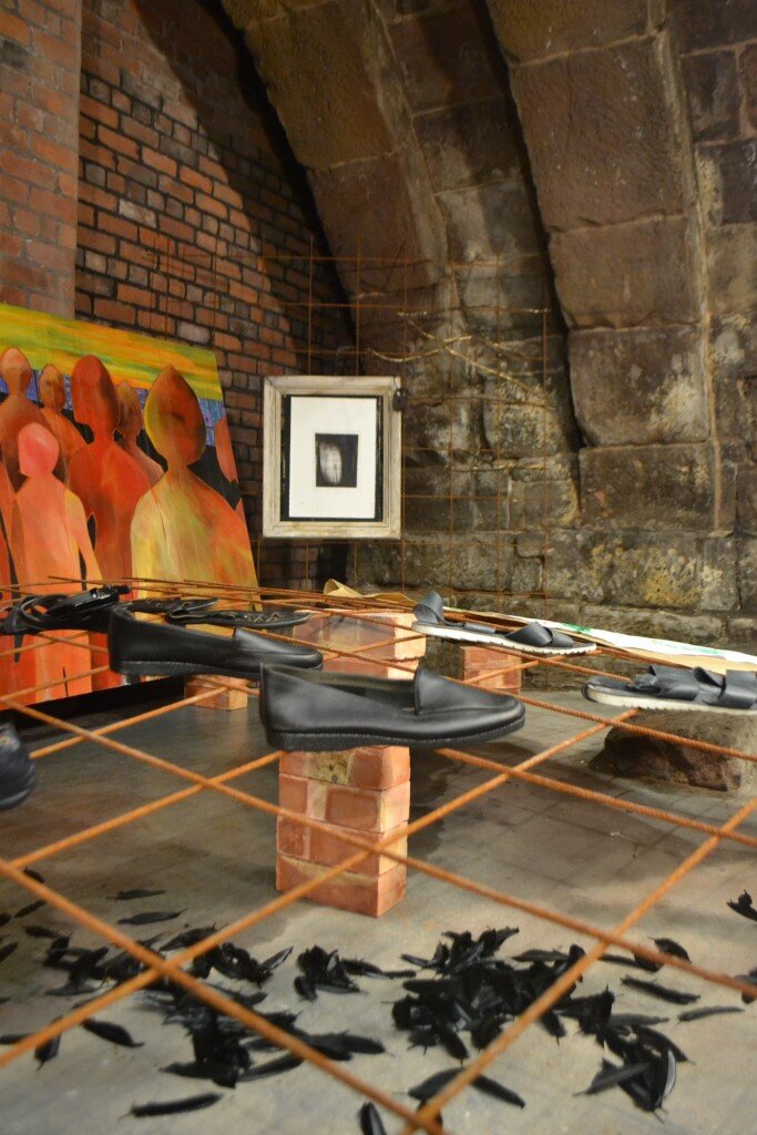 Overhead view of the To Walk In Beauty installation beneath the vaulted stone Hanging Bridge, with small framed prints and scattered black feather forms