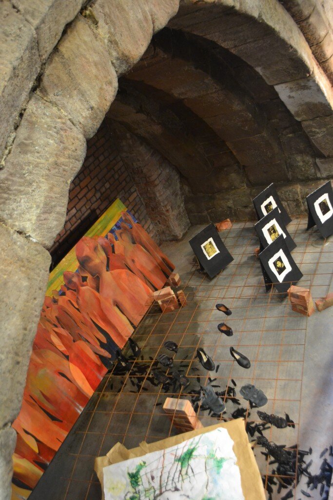 Shoes displayed on brick pedestals within a rusted metal grid, part of the To Walk In Beauty installation
