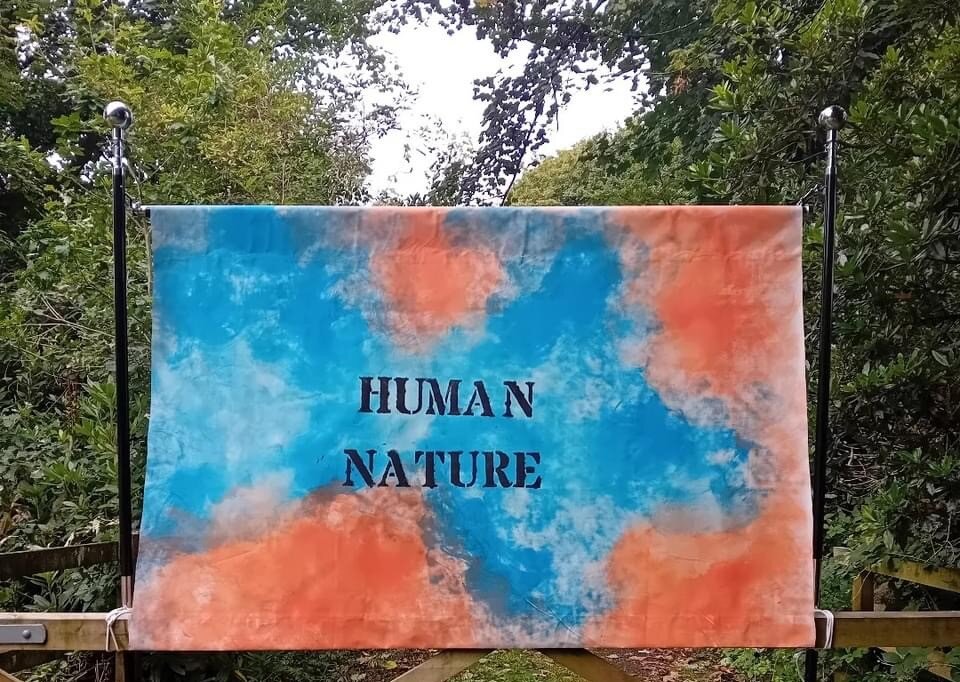 Human Nature exhibition banner in orange and blue, hung at the entrance to the trail