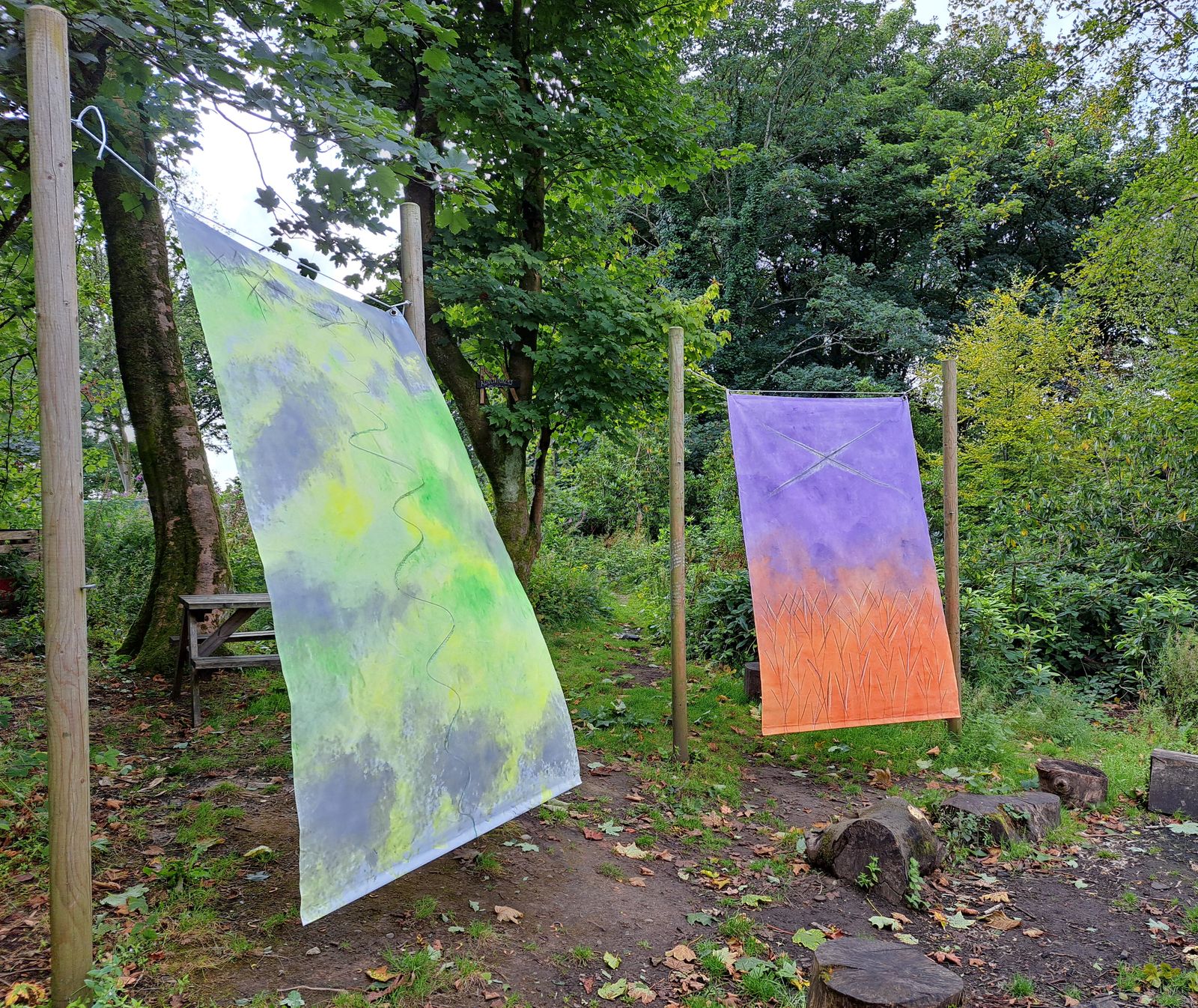 Purple and green hand-dyed fabric hangings suspended outdoors in woodland, part of the Human Nature trail