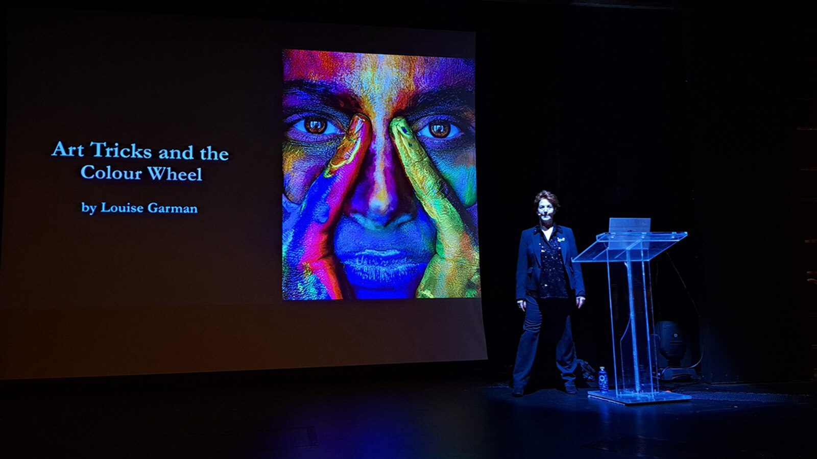 Louise Garman presenting Art Tricks and the Colour Wheel, with a colour-wheel face portrait on screen