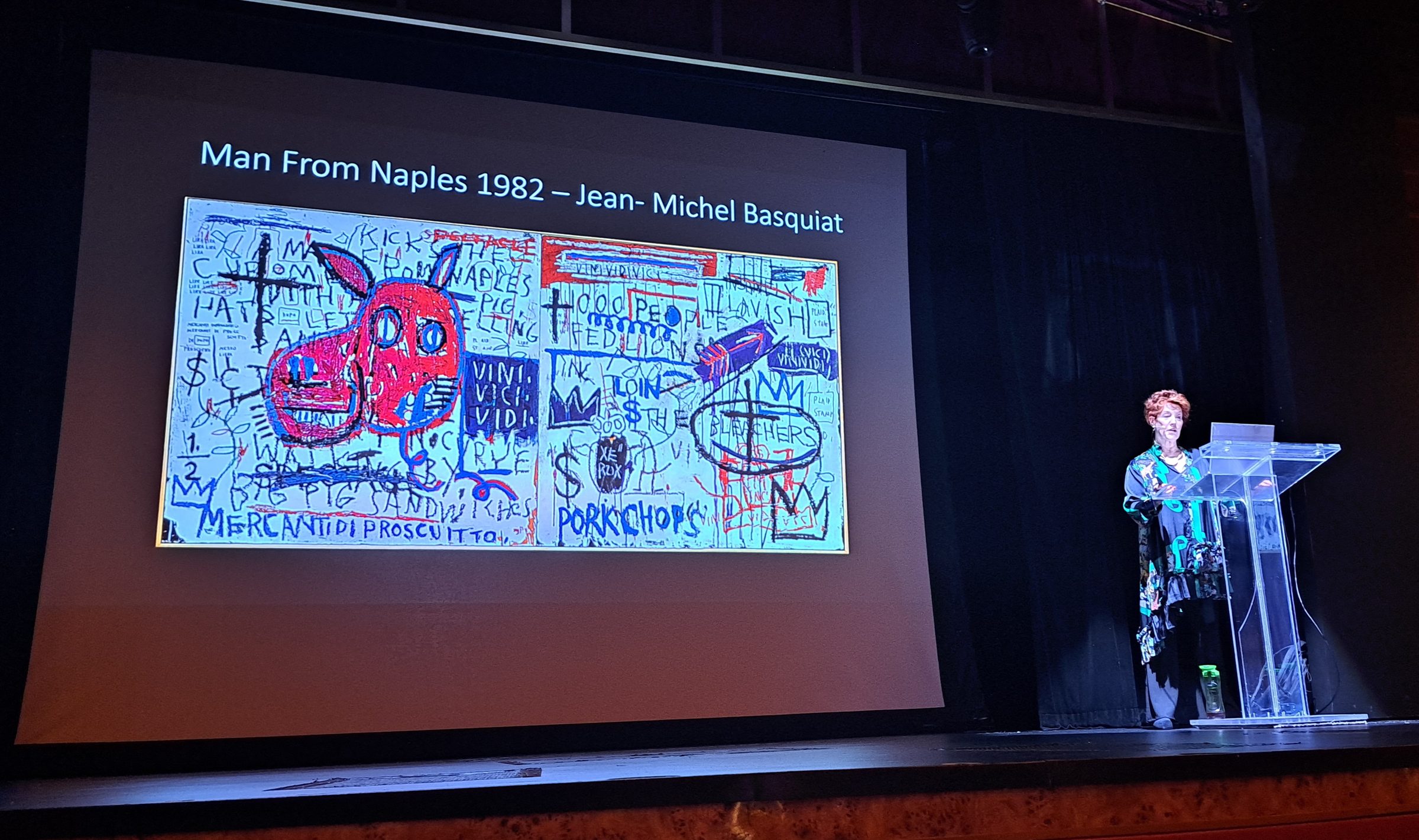 Louise Garman on stage beside a screen showing Jean-Michel Basquiat's Man From Naples, 1982, during her Guggenheim Bilbao talk